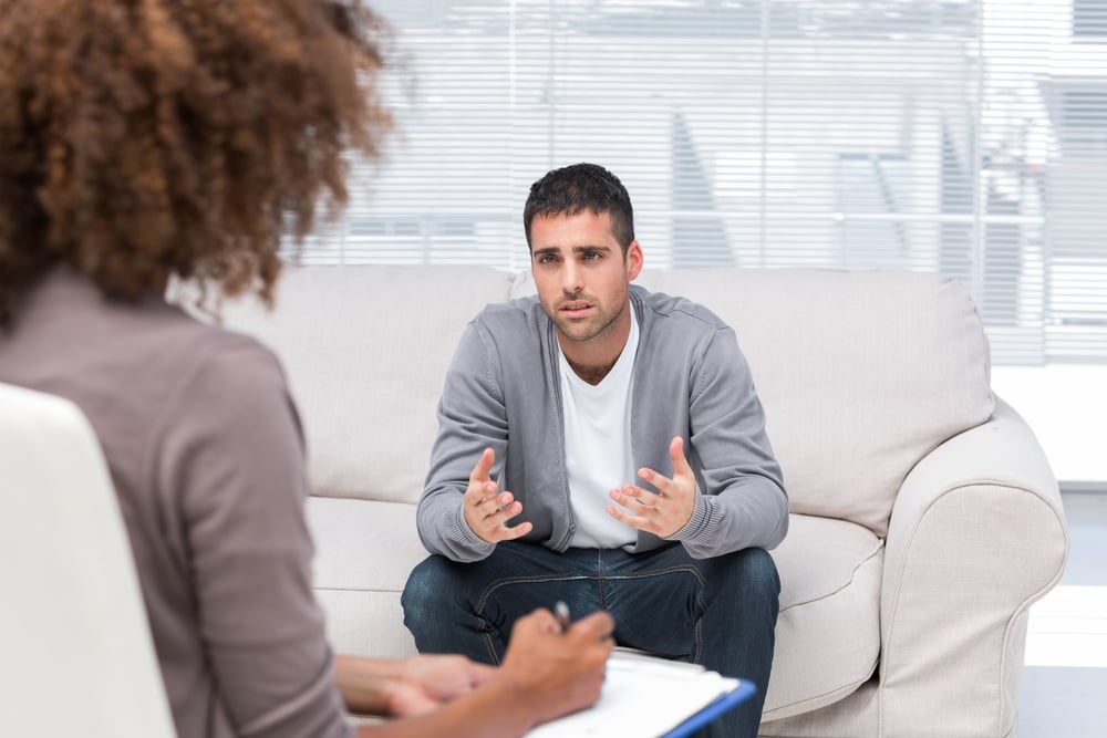 Depressed man speaking to a therapist while she is taking notes