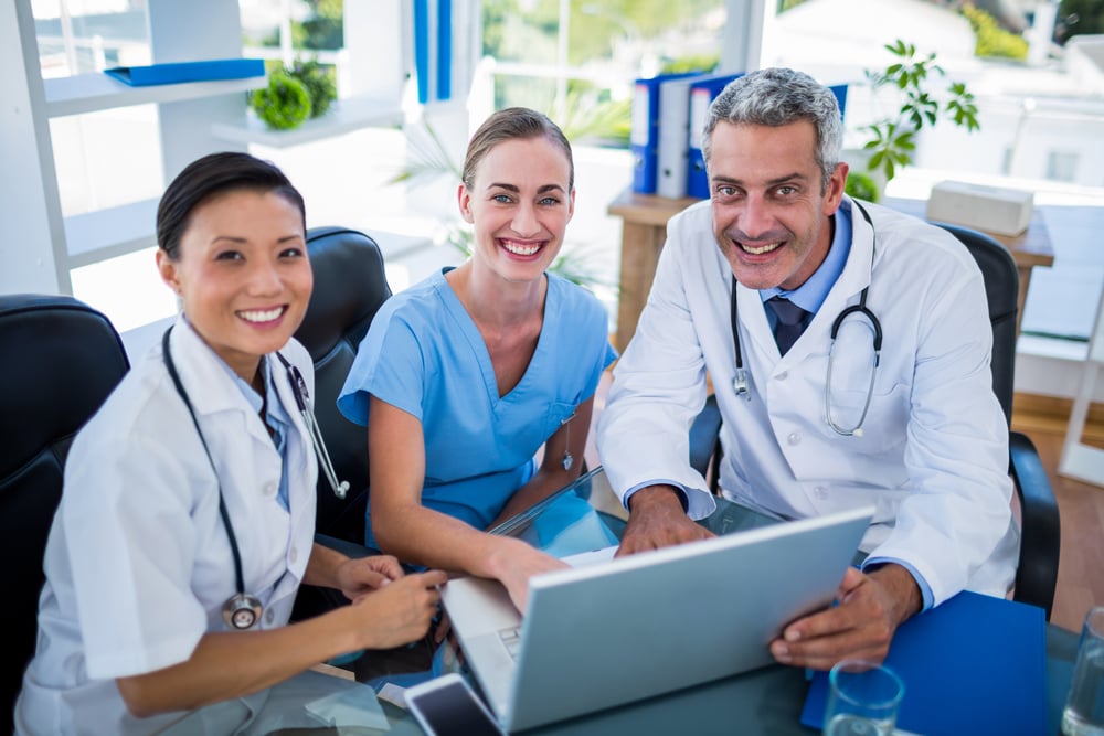 Doctors and nurse looking at laptop and smiling at camera in medical office