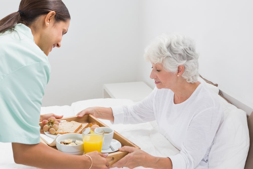 Elderly woman taking a breakfast with home nurse in the bedroom